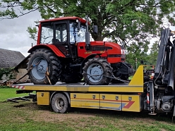 Evakuators, kas paceļ lielu traktoru no lauku teritorijas.