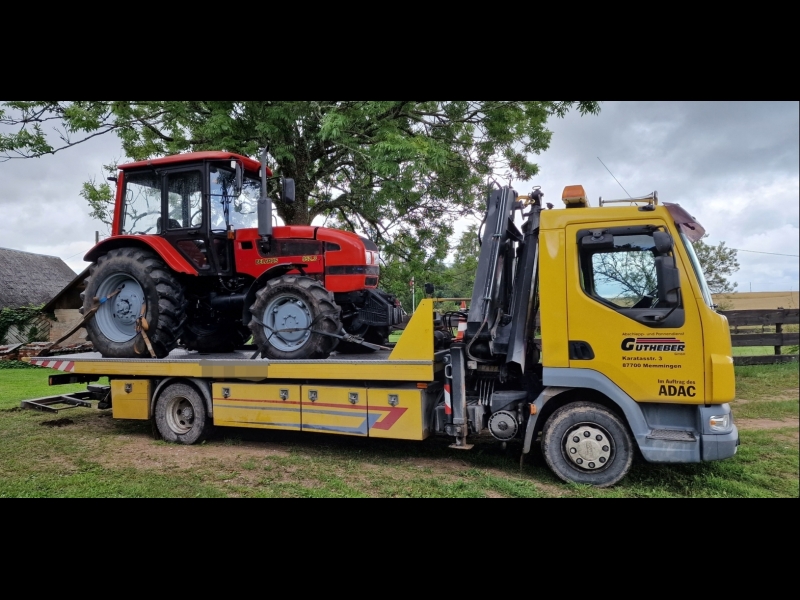 Evakuators, kas paceļ lielu traktoru no lauku teritorijas.