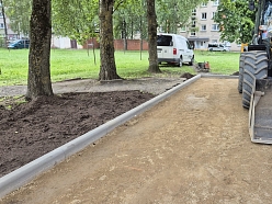 kskavators izlīdzina zemi ap jauniem ietves elementiem