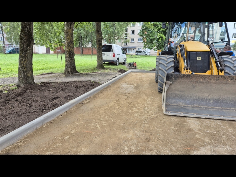 kskavators izlīdzina zemi ap jauniem ietves elementiem